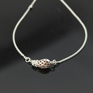 Puede incluir: Un collar de cadena de plata con un pequeño colgante marrón en forma de jaula.