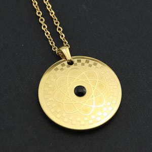 Peut inclure: Un collier en or avec un pendentif rond représentant un symbole d'atome et une pierre noire au centre.
