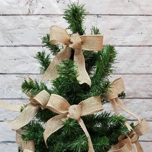 May include: A small artificial Christmas tree decorated with multiple burlap bows. The bows are tied in a simple knot and have a rustic, natural look.