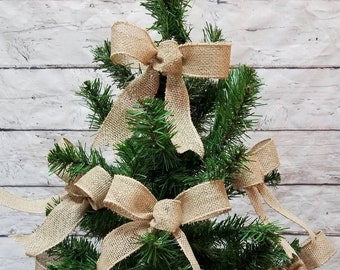 May include: A small artificial Christmas tree decorated with multiple burlap bows. The bows are tied in a simple knot and have a rustic, natural look.
