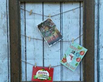 May include: A rustic brown wood picture frame with a string and clothespins holding holiday cards. The cards feature a wreath, a snowman, and the text "Merry Bright" and "Happy Holidays".