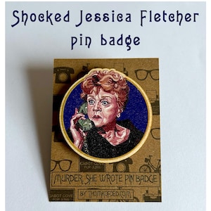 May include: A pin badge featuring a portrait of Jessica Fletcher from Murder, She Wrote, with the text "Shocked Jessica Fletcher pin badge." The badge is 5cm x 5cm and made of birch-faced poplar.