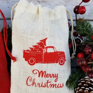 Pu&ograve; includere: Un sacchetto di iuta color crema con coulisse e un camion rosso vintage che trasporta un albero di Natale. Le parole "Merry Christmas" sono stampate in rosso sotto. Il sacchetto ha un cordoncino color naturale.