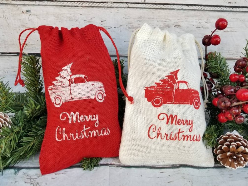 Pu&ograve; includere: Due sacchetti regalo in iuta con coulisse. Uno &egrave; rosso, l'altro naturale. Ogni sacchetto presenta un camion vintage che trasporta un albero di Natale, con "Merry Christmas" stampato sotto. Decorazioni festive natalizie.