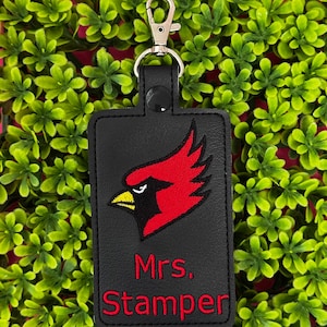 May include: Black rectangular keychain with a red cardinal bird design and the name "Mrs. Stamper" embroidered in red. The keychain has a silver-colored clasp and a black snap closure.