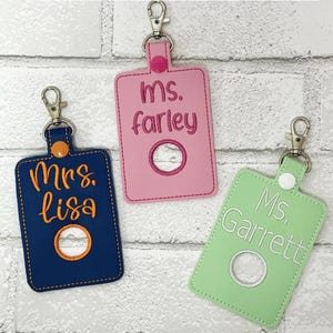 May include: Three rectangular keychains with metal lobster clasps and snap buttons. The navy one features orange embroidery reading Mrs. Lisa, the pink one has dark pink embroidery reading ms. farley, and the light green one has white embroidery reading Ms. Garrett.