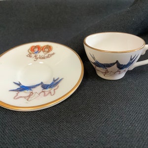 Puede incluir: Un juego de taza y platillo de té blanco con ribete dorado. El platillo tiene un diseño de pájaro azul con el texto "Be My Valentine". La taza tiene un diseño de pájaro azul.