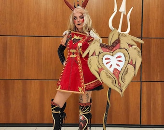 May include: A person in a red and gold costume with a heart-shaped shield and a trident. The costume includes a red dress, black boots with gold accents, and a crown with rabbit ears. The shield is gold with a white heart.