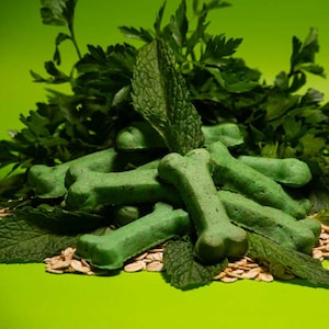 May include: A pile of green dog treats shaped like bones, surrounded by fresh green herbs.