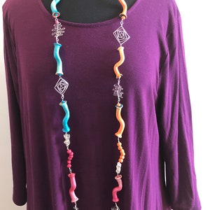 May include: A long necklace featuring blue, orange, and pink ceramic beads, silver wire, and silver geometric shapes.