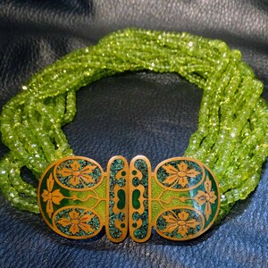 May include: A multi-strand necklace made of green peridot beads with a gold clasp featuring an intricate floral design.