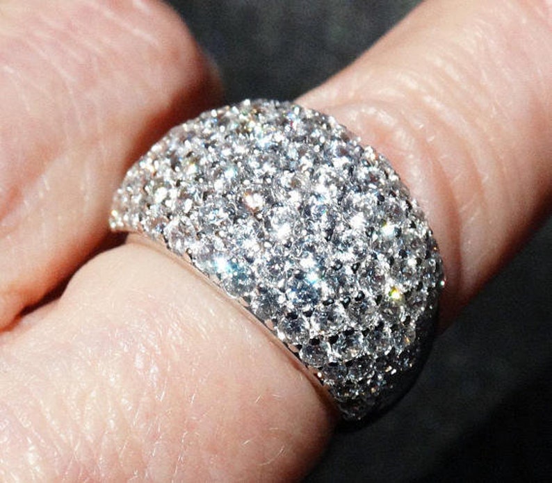 May include: A silver ring with a large, round, pave-set diamond design.