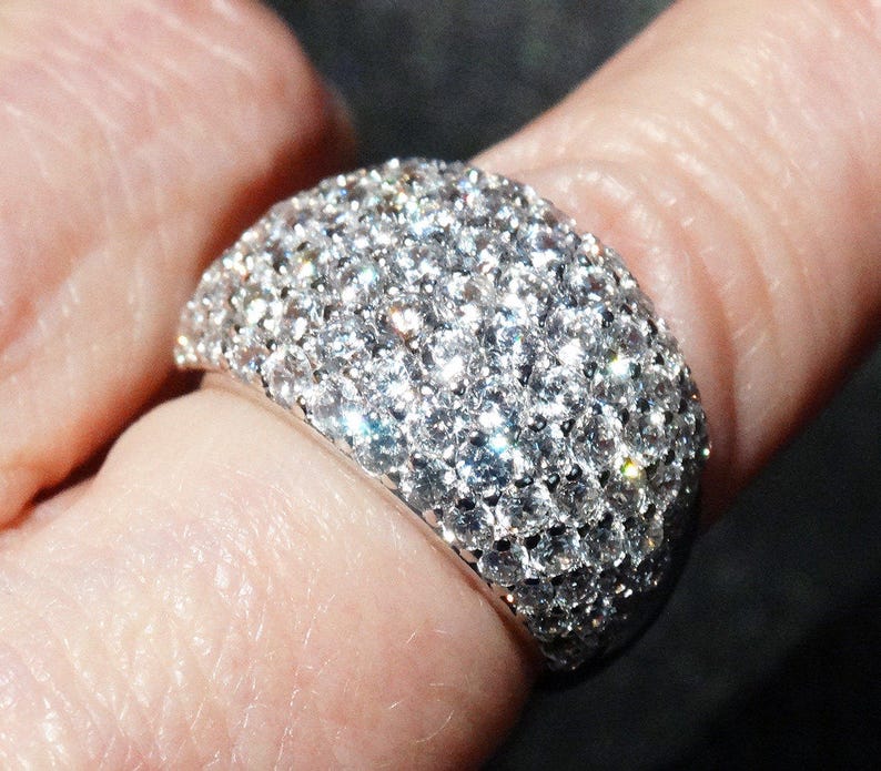 May include: A silver ring with a wide band covered in small, sparkling diamonds.