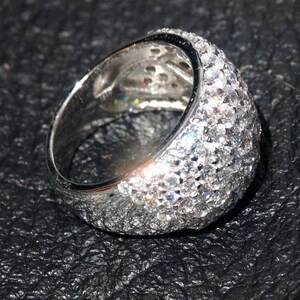 May include: A silver ring with a wide band set with small, clear stones. The stones are set in a pave setting and cover the entire band of the ring.