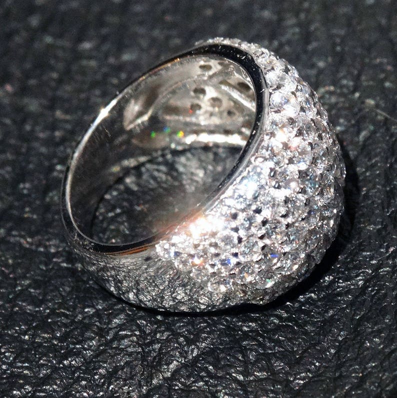 May include: A silver ring with a wide band set with small, clear stones. The stones are set in a pave setting and cover the entire band of the ring.