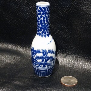 May include: A small, blue and white porcelain vase with a floral design on the neck and a landscape scene on the body. The vase is about 4 inches tall and is sitting on a black surface.