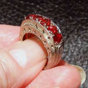 May include: A silver ring with a delicate filigree design and a row of red gemstones.