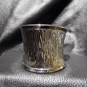 May include: A black ceramic ring holder with a wood grain pattern. The holder has a silver rim.