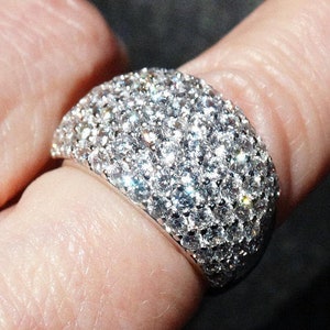 May include: A silver ring with a large, round, pave-set diamond design.
