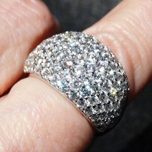 May include: A silver ring with a large, round, pave-set diamond design.