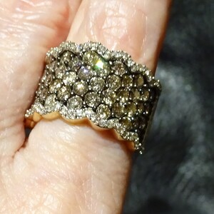 May include: A gold band ring with a wide, wavy design set with multiple rows of small, sparkling brown diamonds.