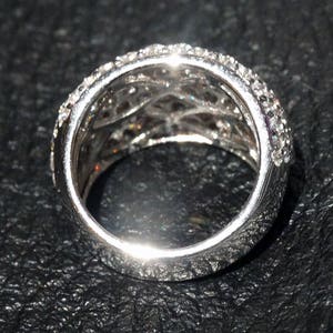 May include: A silver ring with a delicate, multi-layered design. The ring is set with small, clear stones that create a sparkling effect.
