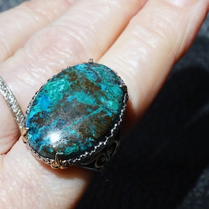 May include: A silver ring with a large oval-shaped turquoise gemstone set in a silver filigree setting.