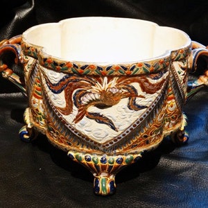 K&ouml;nnte beinhalten: Eine gro&szlig;e, wei&szlig;e Keramikschale mit einem dekorativen Design aus Drachen und Wolken in Blaut&ouml;nen, Gr&uuml;n, Gold und Braun. Die Schale hat drei F&uuml;&szlig;e und zwei Griffe.