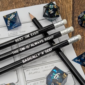 May include: Three black pencils with white text on them. The text on the pencils reads "Best DM Ever", "The DM is Always Right", and "Basically a God". The pencils are on a white sheet of paper with a character sheet for a role-playing game.