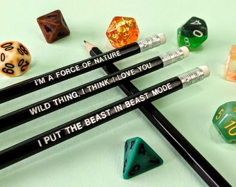 Puede incluir: Lápices negros con texto blanco: "I'M A FORCE OF NATURE", "WILD THING, I THINK I LOVE YOU" y "I PUT THE BEAST IN BEAST MODE". Los lápices están rodeados de dados coloridos.