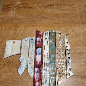 Può includere: Un set di nove piastrelle in ceramica con vari motivi e colori, tra cui bianco, blu, rosso, marrone e nero. Le piastrelle sono disposte a ventaglio e hanno una superficie testurizzata.
