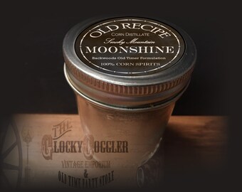 May include: A glass jar with a silver lid and a brown label that reads "OLD RECIPE CORN DISTILLATE Smoky Mountain MOONSHINE Backwoods Old Timer Formulation 100% CORN SPIRITS". The jar is sitting on a wooden surface.