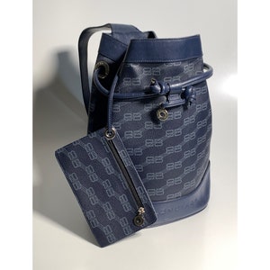 Puede incluir: Un bolso de cubo de cuero azul marino con cierre de cordón y una bolsa con cremallera a juego. El bolso presenta un patrón de eslabón de cadena repetido y el nombre de la marca "BENDASI" es visible en la parte inferior.