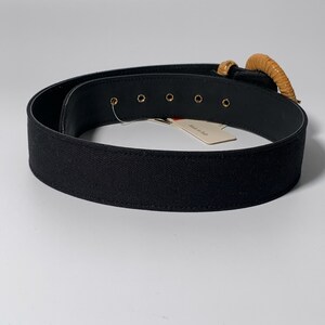 May include: Black canvas belt with a large, round, brown buckle. The buckle has a gold metal accent. The belt has five gold metal eyelets. The tag on the belt reads "Made in Italy".
