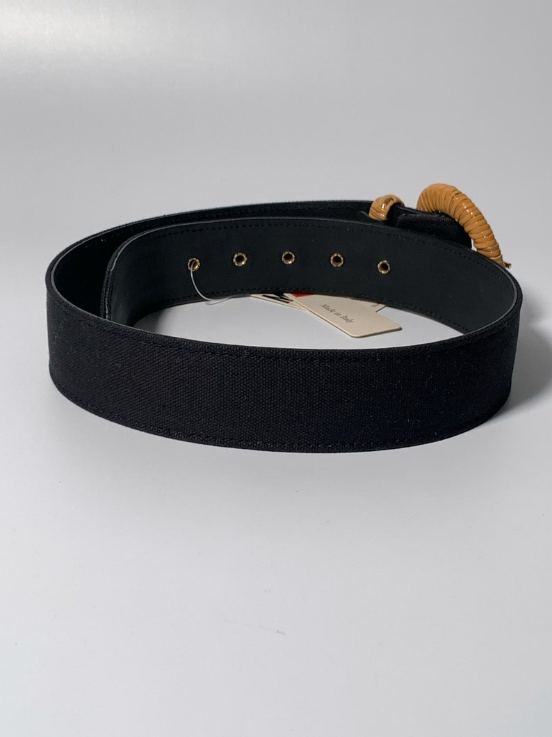 May include: Black canvas belt with a large, round, brown buckle. The buckle has a gold metal accent. The belt has five gold metal eyelets. The tag on the belt reads "Made in Italy".