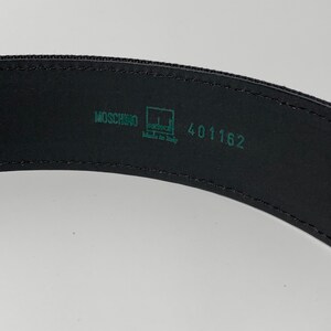 May include: Black leather belt with a green label that reads "Moschino" and "Made in Italy" with the number "401162" printed on the label.