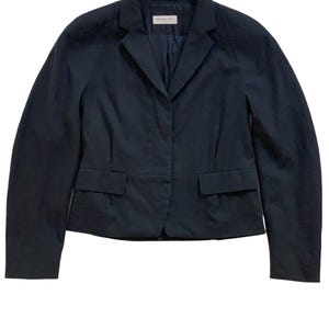 Puede incluir: Un blazer azul marino con un diseño clásico. La chaqueta presenta solapas con muescas, dos bolsillos delanteros y un cierre de un solo botón. El blazer está hecho de una tela suave y ligera.