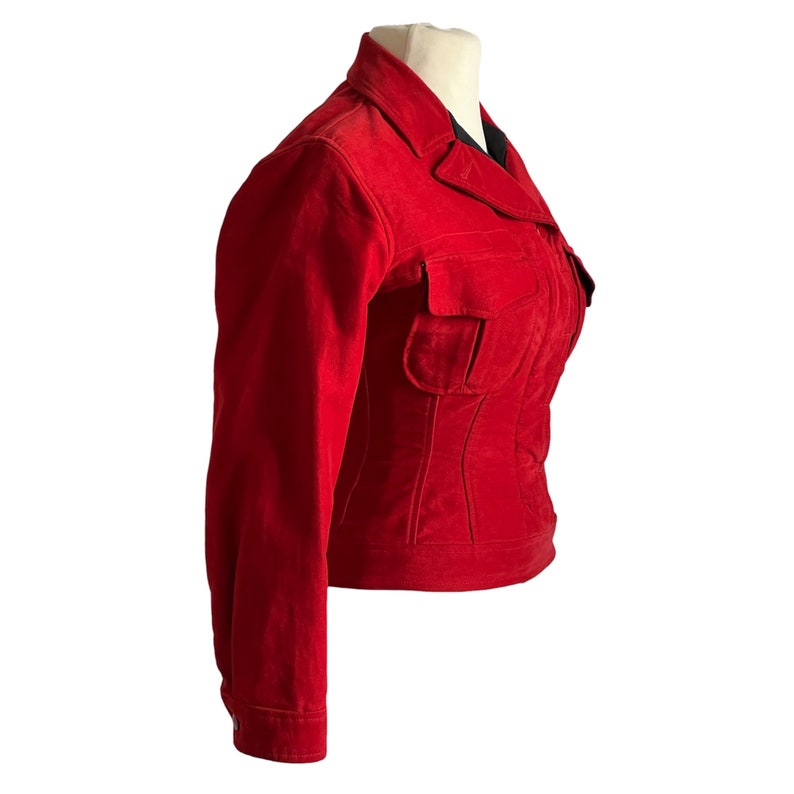 May include: A red corduroy jacket with a zipper closure and a large pocket on the front. The jacket has a fitted silhouette and long sleeves.