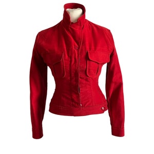 May include: A red velvet jacket with a high collar, long sleeves, and two large pockets on the front. The jacket has a button closure and a fitted waist.