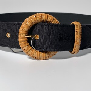 May include: A black canvas belt with a large, round, woven, light brown buckle. The buckle has a gold metal ring.