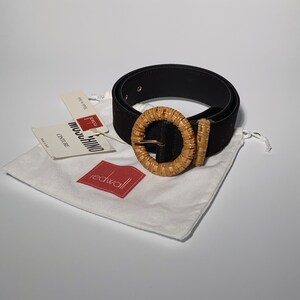 May include: Black suede belt with a woven, light brown, circular buckle. The belt is packaged in a white drawstring bag with a red "Redwall" logo.