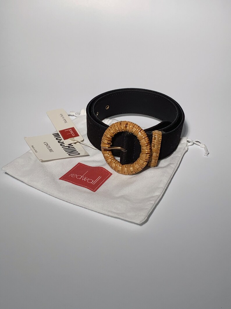 May include: Black suede belt with a woven, light brown, circular buckle. The belt is packaged in a white drawstring bag with a red "Redwall" logo.