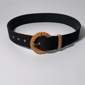 May include: A black woven belt with a large, round, woven buckle. The buckle is a light brown color.