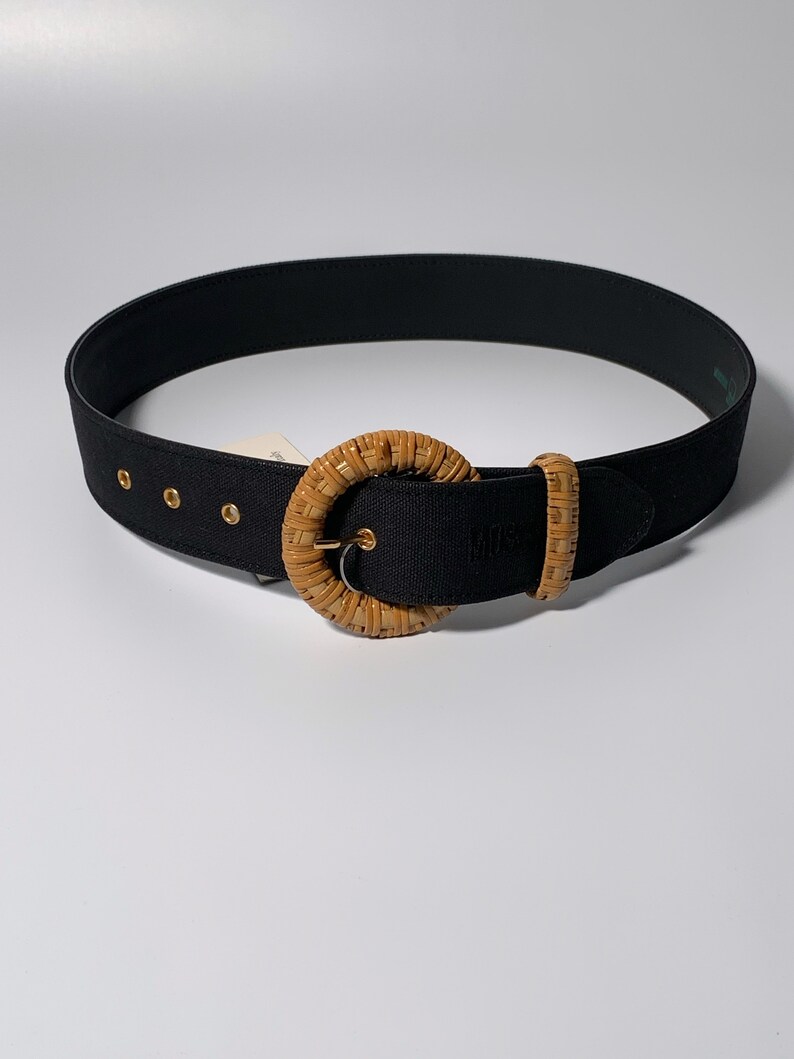 May include: A black woven belt with a large, round, woven buckle. The buckle is a light brown color.
