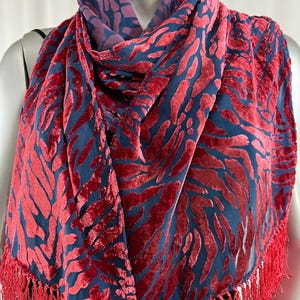 May include: A red and blue patterned scarf with a fringe border. The scarf is made of a soft, velvety material.