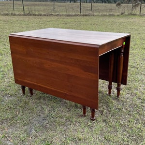 May include: A dark wood drop leaf table with turned legs. The table is closed and has a rectangular top. The table is sitting on a grassy field.