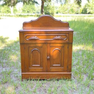 May include: A vintage wooden cabinet with a single drawer and two doors. The cabinet has a dark brown finish and intricate carvings on the front.