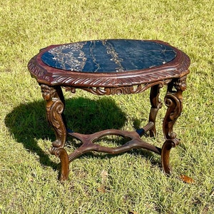 May include: A dark wood end table with an oval black marble top. The table has intricate carvings on the legs and a decorative stretcher.
