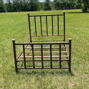 May include: A rusty metal bed frame with a simple design, sitting on a grassy field.