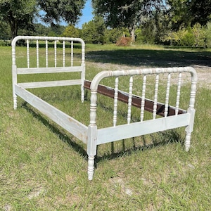 May include: White painted wooden bed frame with a spindle design. The bed frame is in a grassy field.